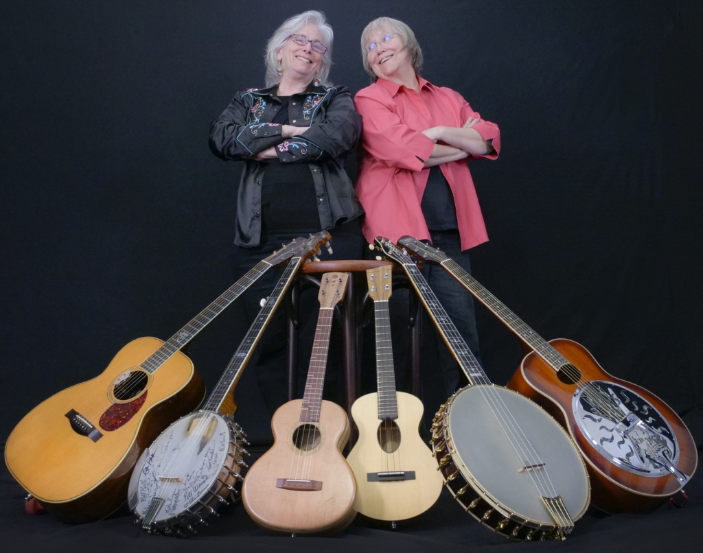 Cathy Fink and Marcy Marxer standing in front a row of stringed instruments.