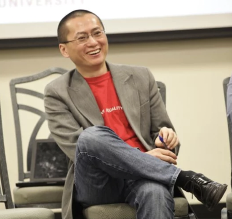 Curtis Chin sitting in a chair while speaking at a conference.